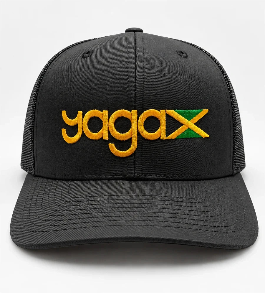Front view of the black YAGA Jamaican Roots Trucker Hat with gold YAGA logo embroidery and an embroidered Jamaican flag above the curved brim.