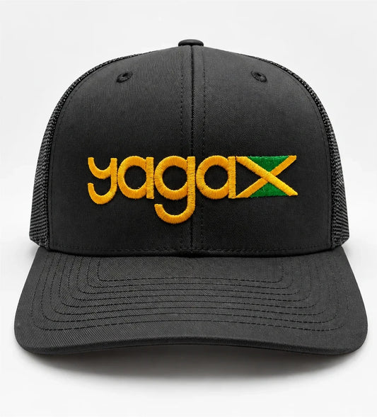 Front view of the black YAGA Jamaican Roots Trucker Hat with gold YAGA logo embroidery and an embroidered Jamaican flag above the curved brim.